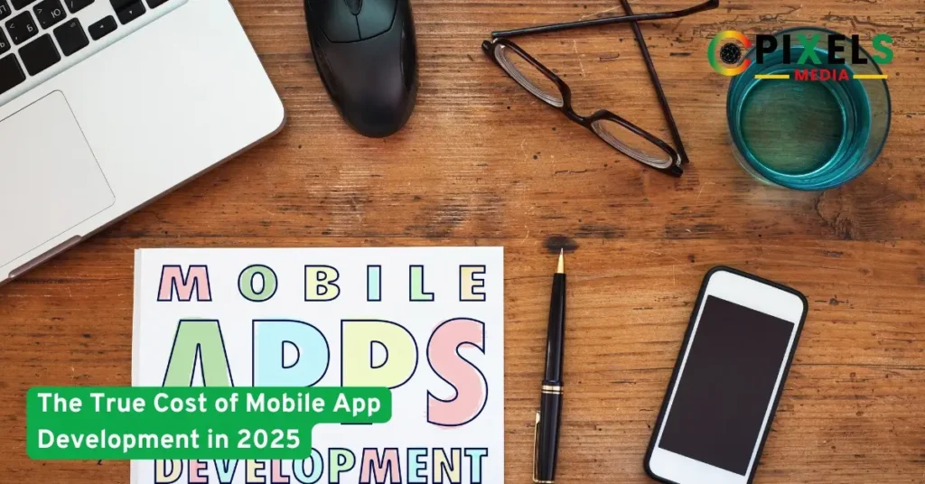 Desk with laptop, smartphone, glasses, and a mobile apps booklet representing the true cost of mobile app development in 2025